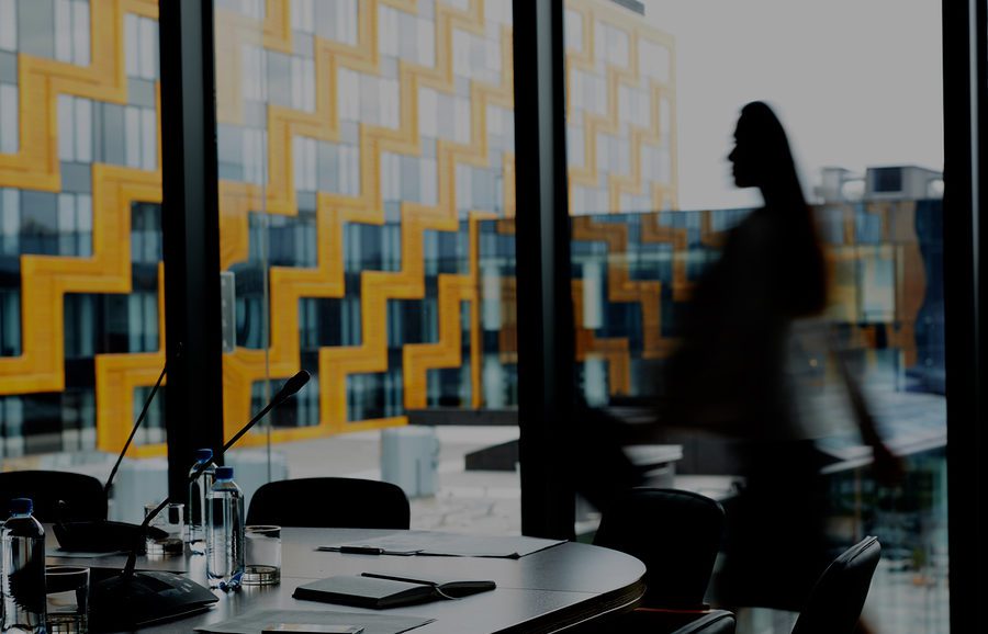 Background image of conference room in modern office with blurred shape of businesswoman crossing it